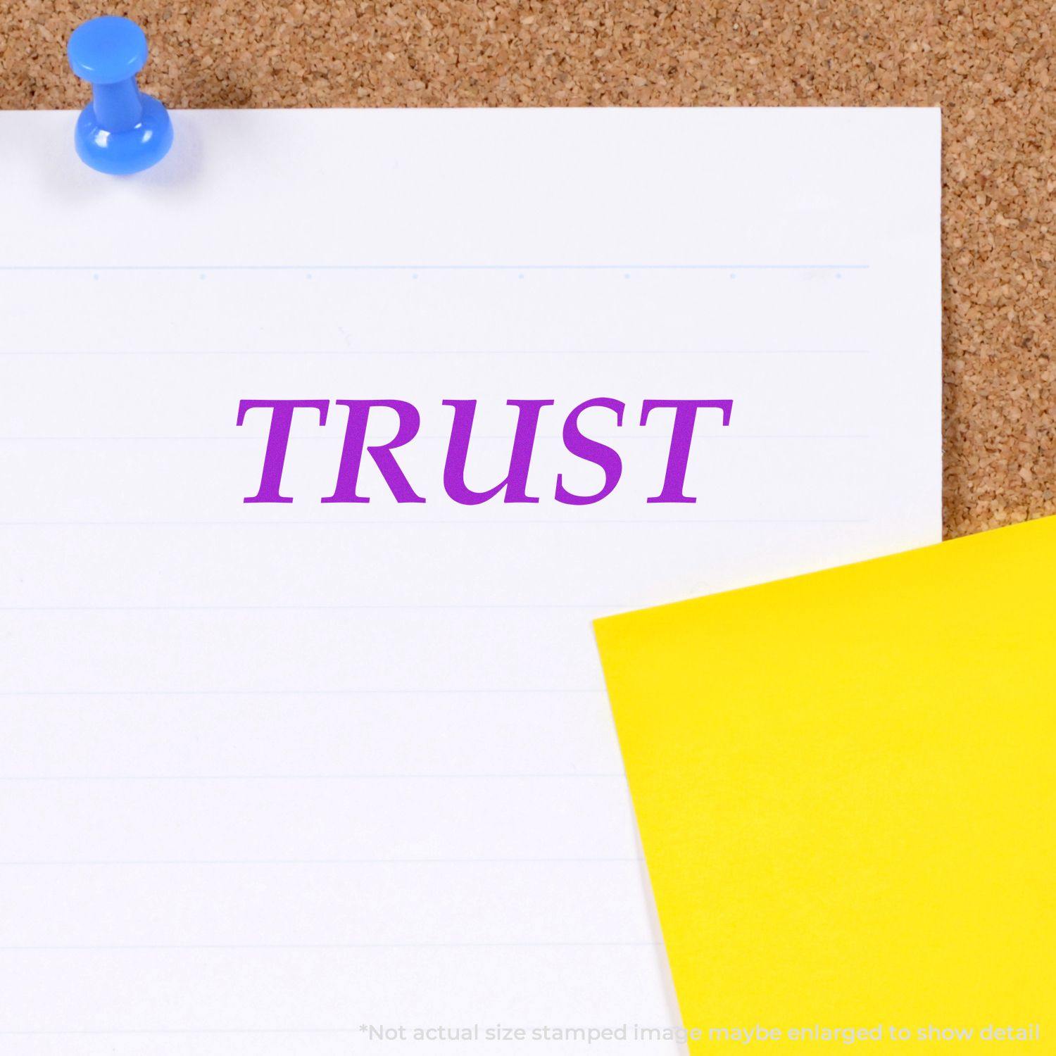 Large Pre-Inked Trust Stamp in purple ink on white paper pinned to a corkboard, with a yellow sticky note partially visible.