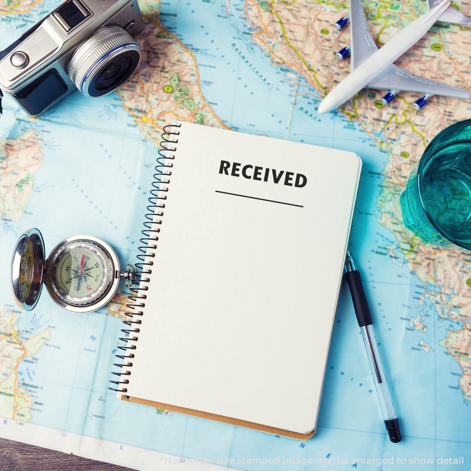 Notebook with RECEIVED stamped using a large two line received rubber stamp, placed on a map with a camera, compass, and pen.