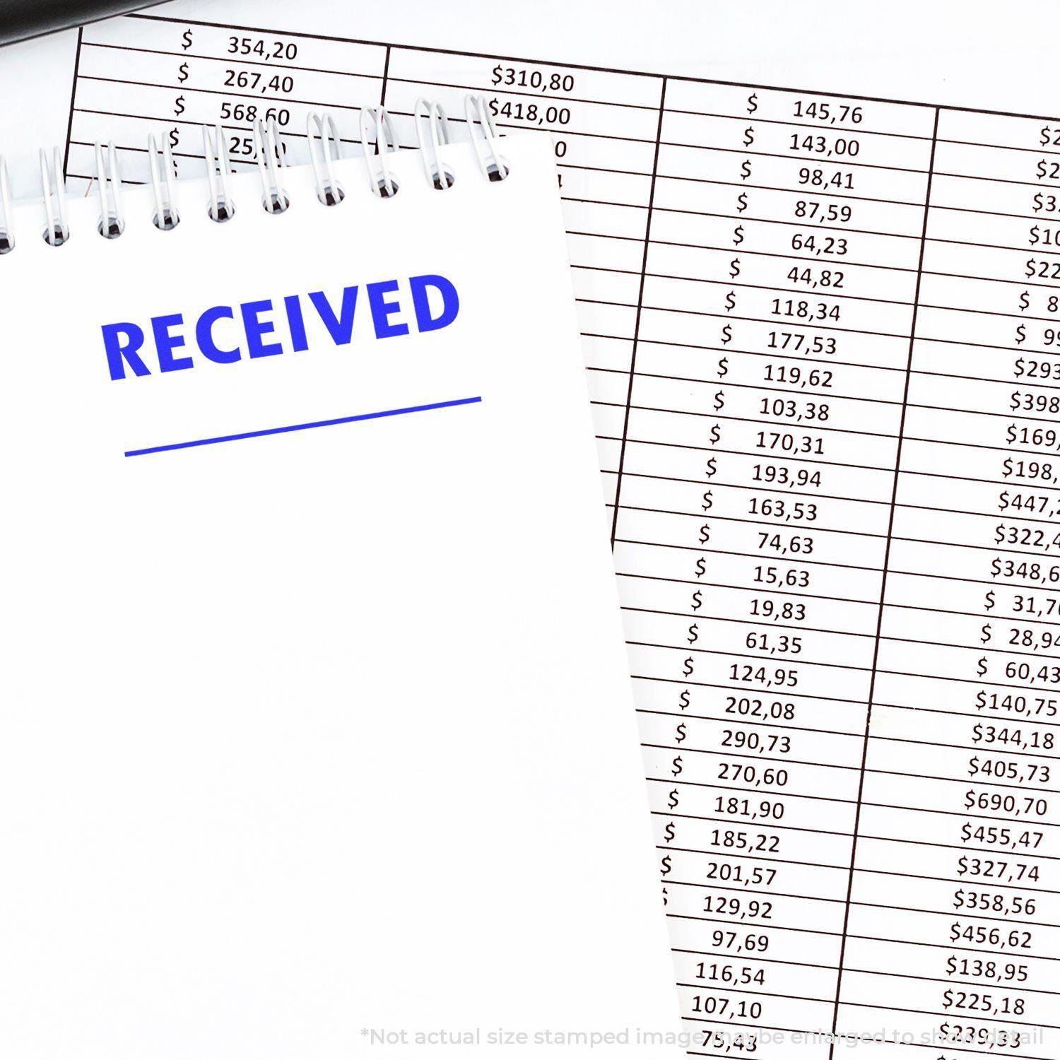 Two Line Received Rubber Stamp in blue ink on a notepad, next to a financial spreadsheet with various dollar amounts.