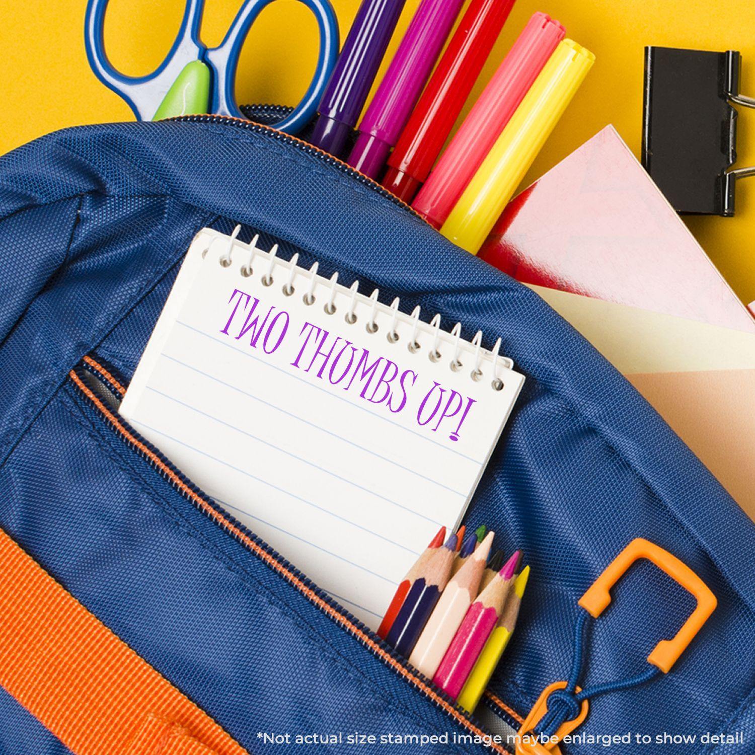 Large Two Thumbs Up Rubber Stamp on a notepad inside a blue backpack with colored pencils, scissors, and other stationery items.