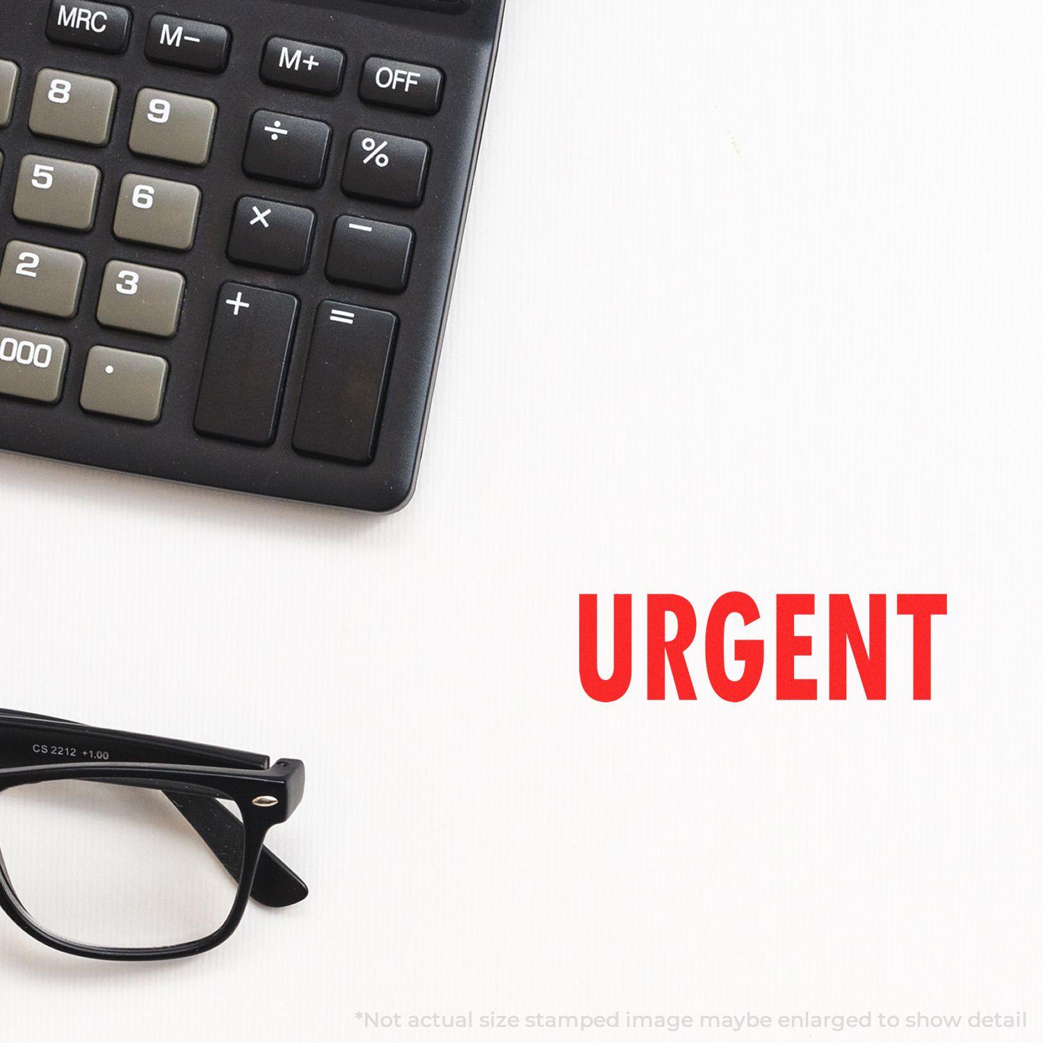 Large urgent rubber stamp marked URGENT in red ink next to a calculator and a pair of glasses on a white surface.