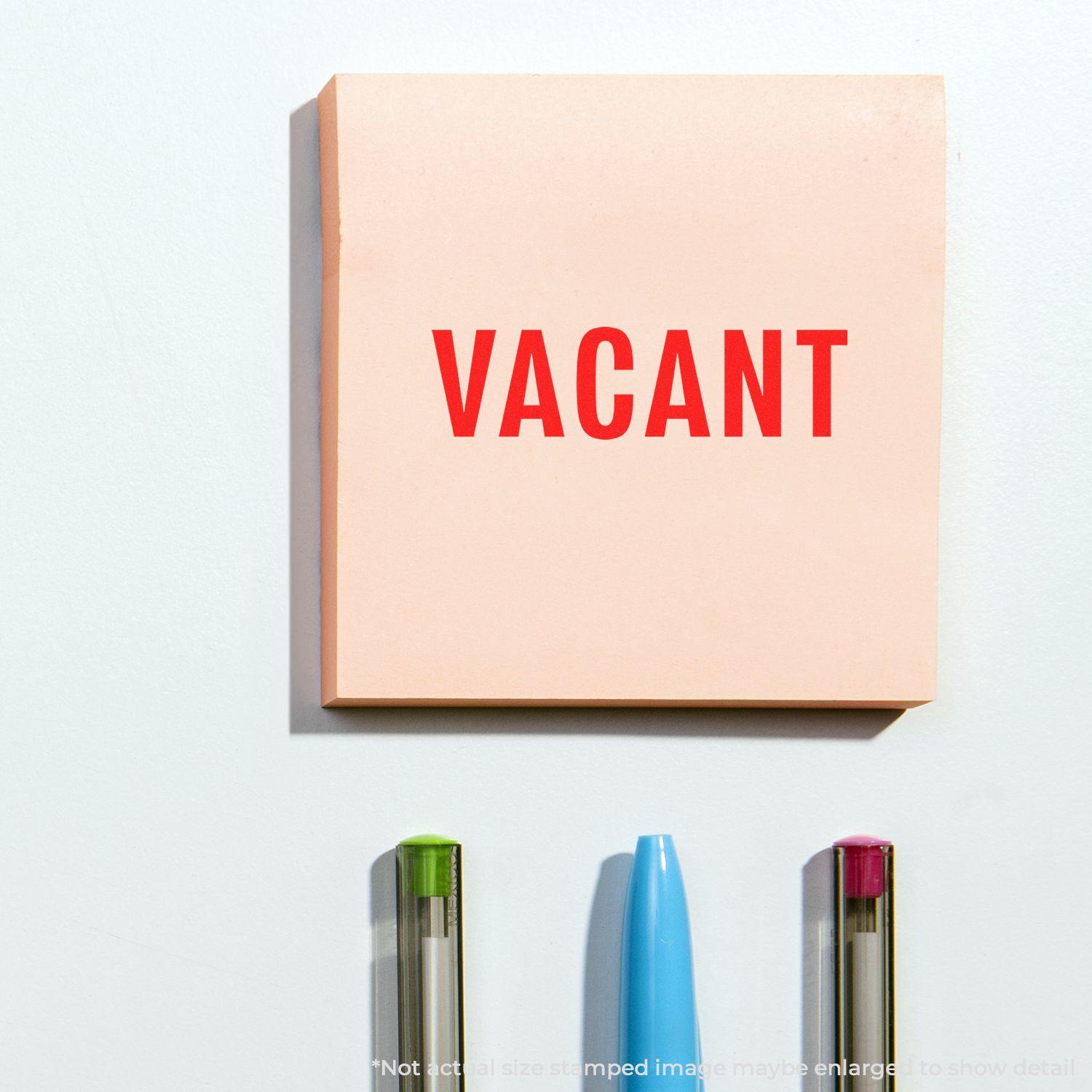 Self Inking Vacant Stamp marking VACANT on a pink sticky note, with three pens below.