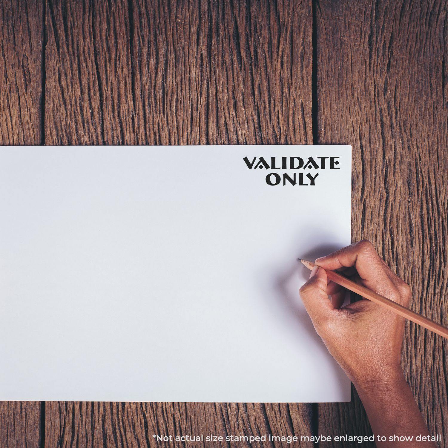 Hand holding a pencil next to a stamped VALIDATE ONLY mark on white paper using the Self Inking Validate Only Stamp on a wooden surface.