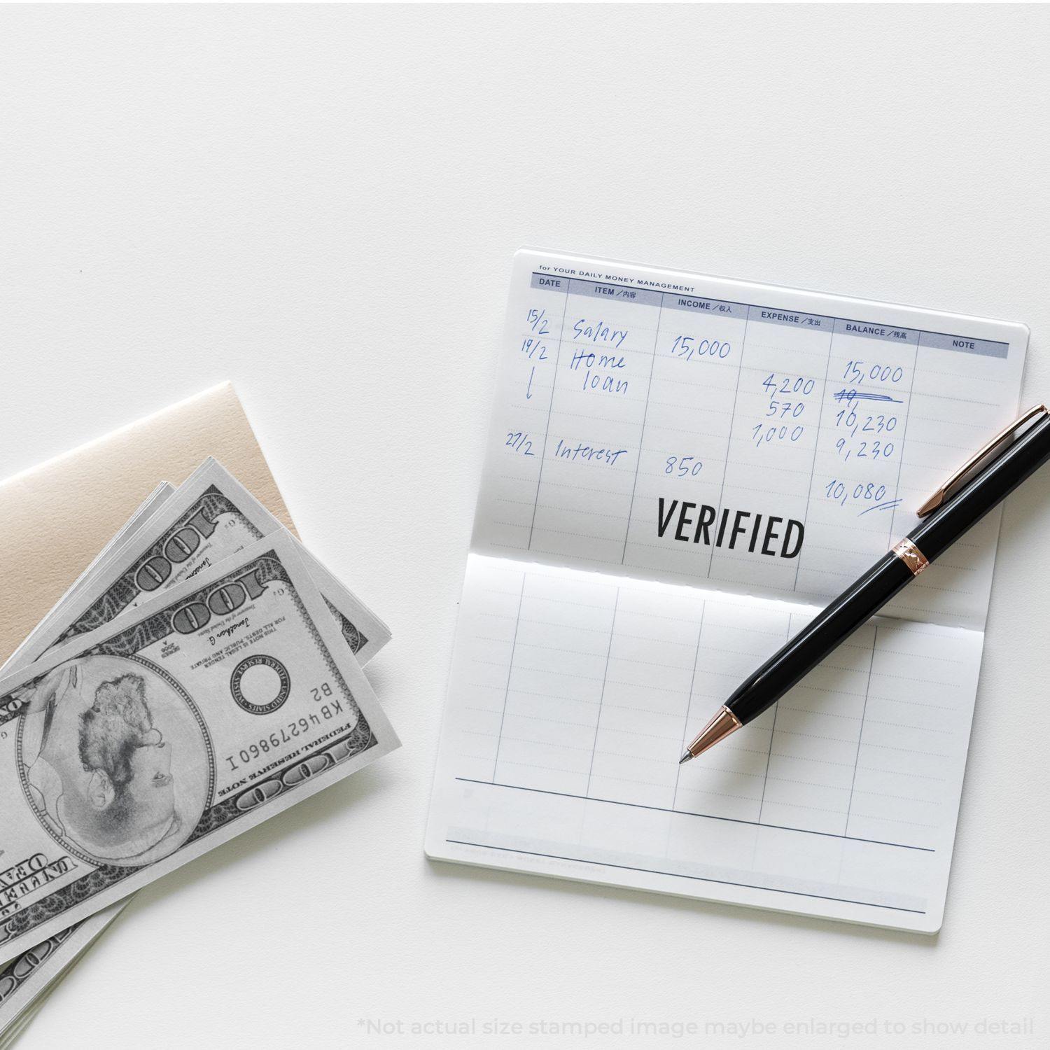 Large Pre-Inked Verified Stamp used on a financial ledger next to a pen, envelope, and stack of dollar bills.