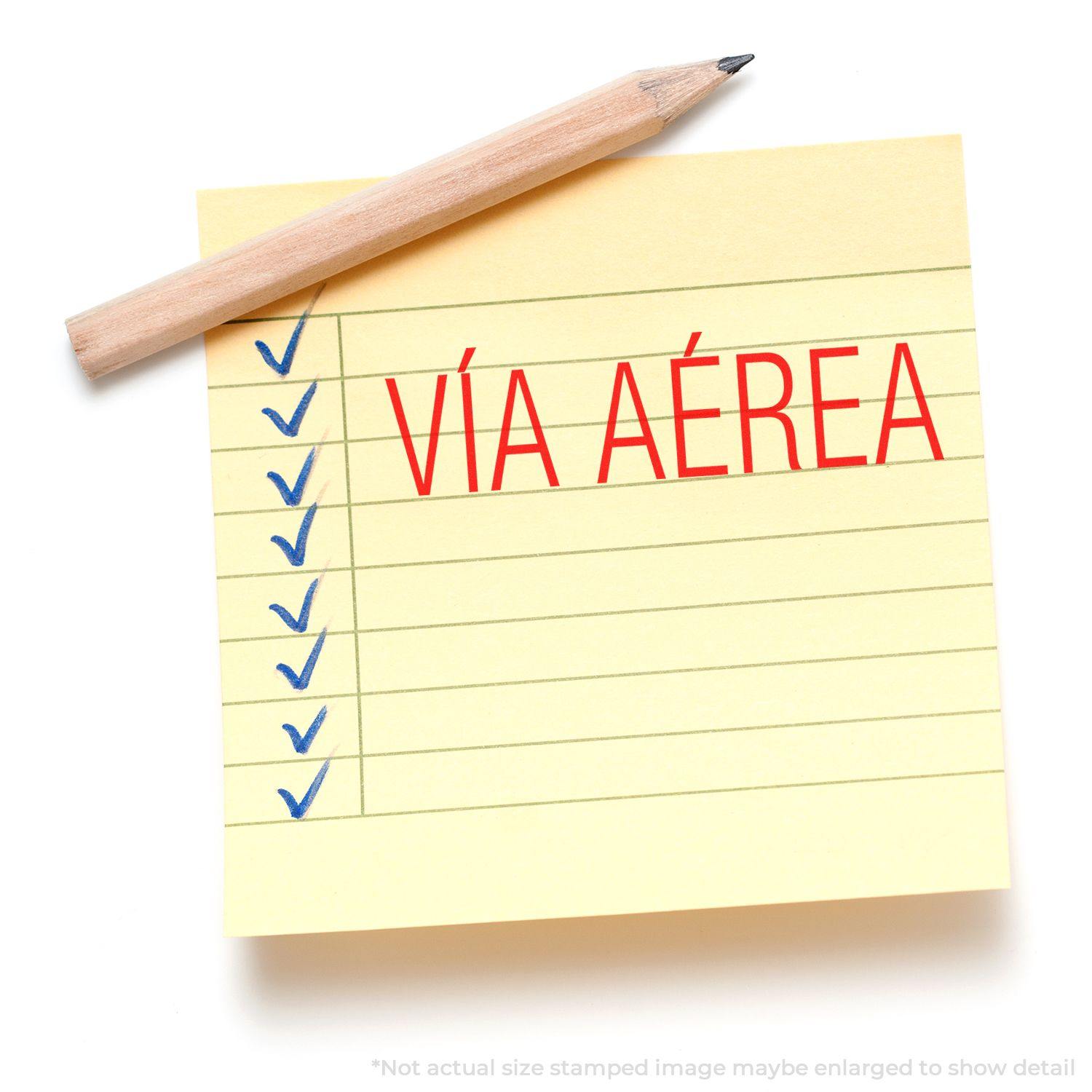 Yellow notepad with blue checkmarks and a Vía Aérea rubber stamp in red ink, accompanied by a wooden pencil.