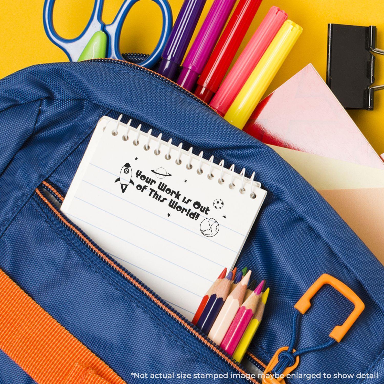 A blue backpack with colored pencils, markers, and a notebook stamped with Your Work is Out of This World using the Large Pre-Inked Stamp.