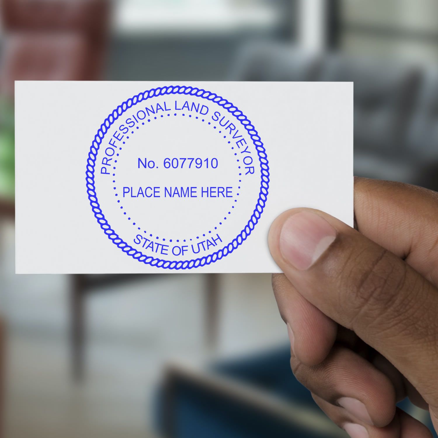 A hand holding a card with a blue Digital Utah Land Surveyor Stamp, Electronic Seal for Utah Land Surveyor, in an office setting.