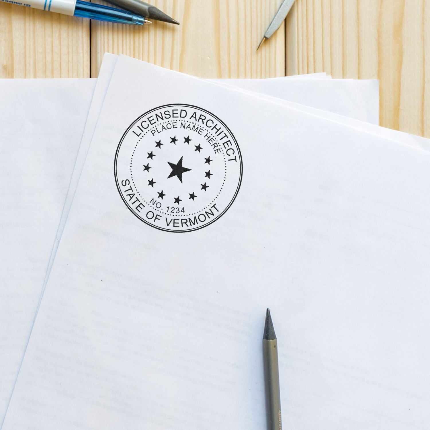 Vermont Architect Seal Stamp on a stack of white papers with pens and a pencil on a wooden surface.