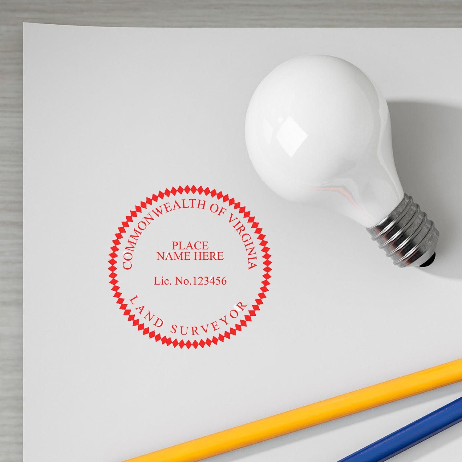 Premium MaxLight Pre-Inked Virginia Surveyors Stamp in red ink on white paper, next to a light bulb and two pencils.