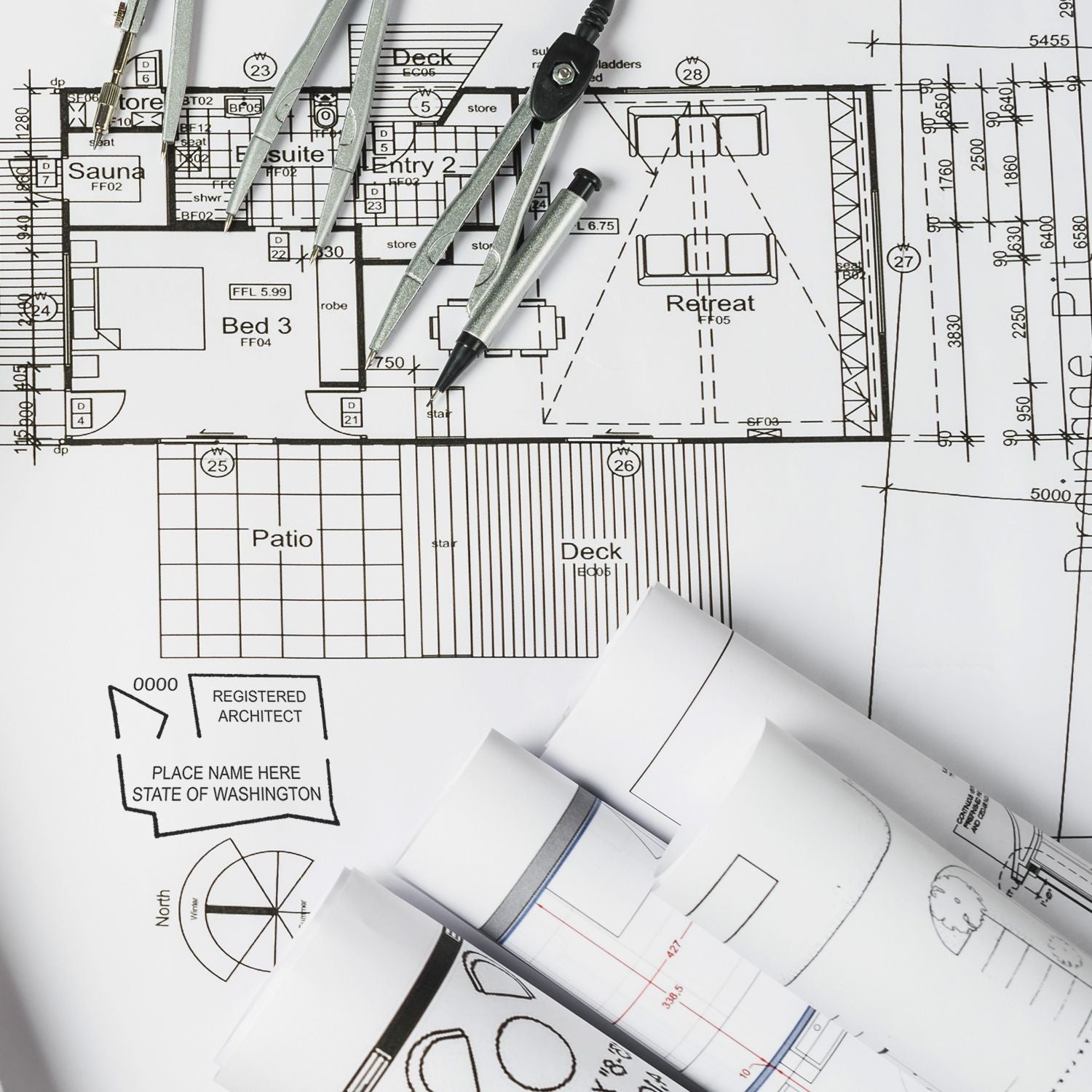 Architectural plans with a Self Inking Washington Architect Stamp, compass, and rolled blueprints on a drafting table.