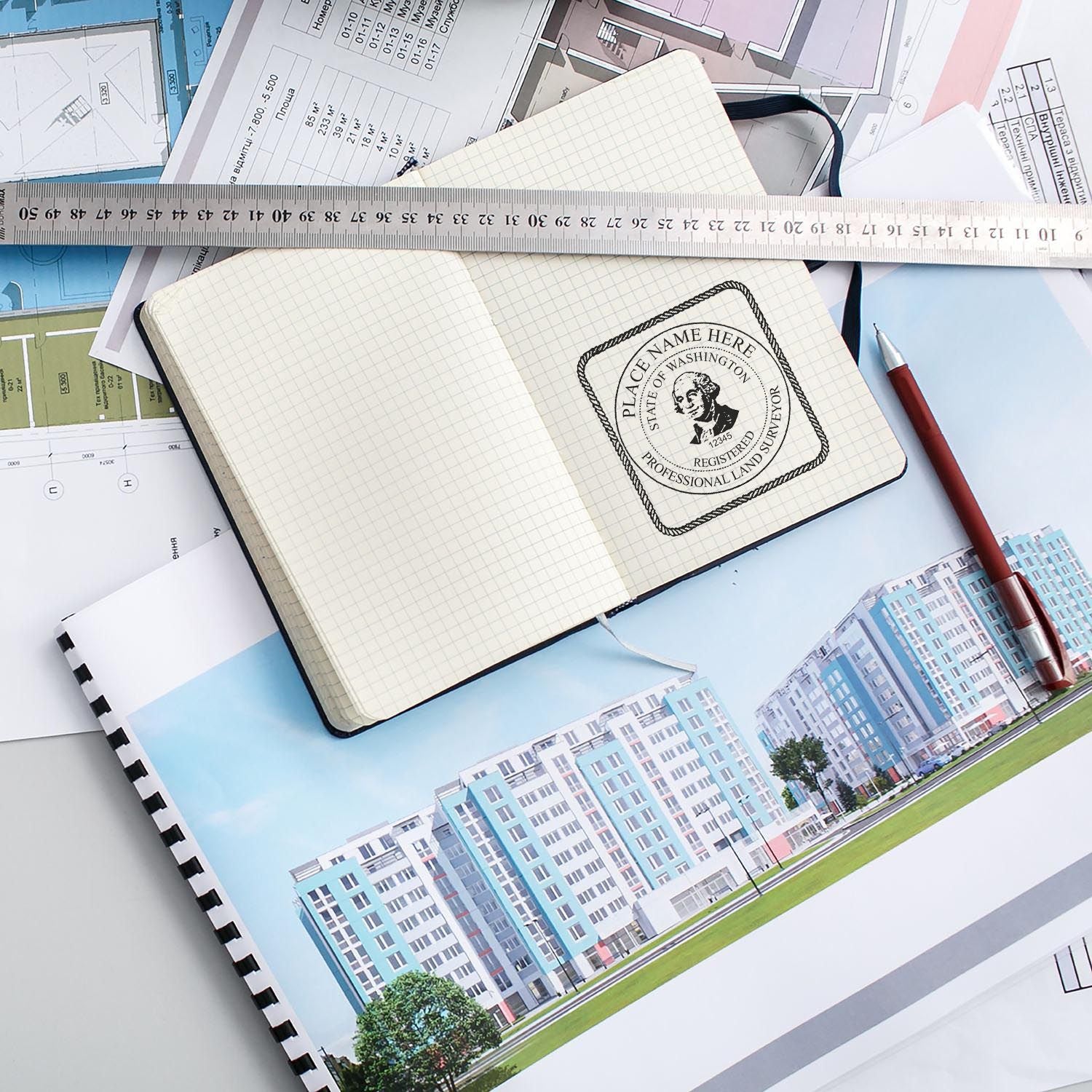 Washington Land Surveyor Seal Stamp in use on a notebook, surrounded by architectural plans, a ruler, and a red pen.