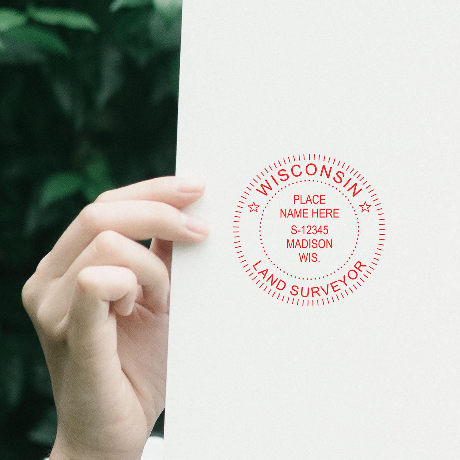 Hand holding a document stamped with the Self Inking Wisconsin Land Surveyor Stamp in red ink, featuring customizable name and location details.