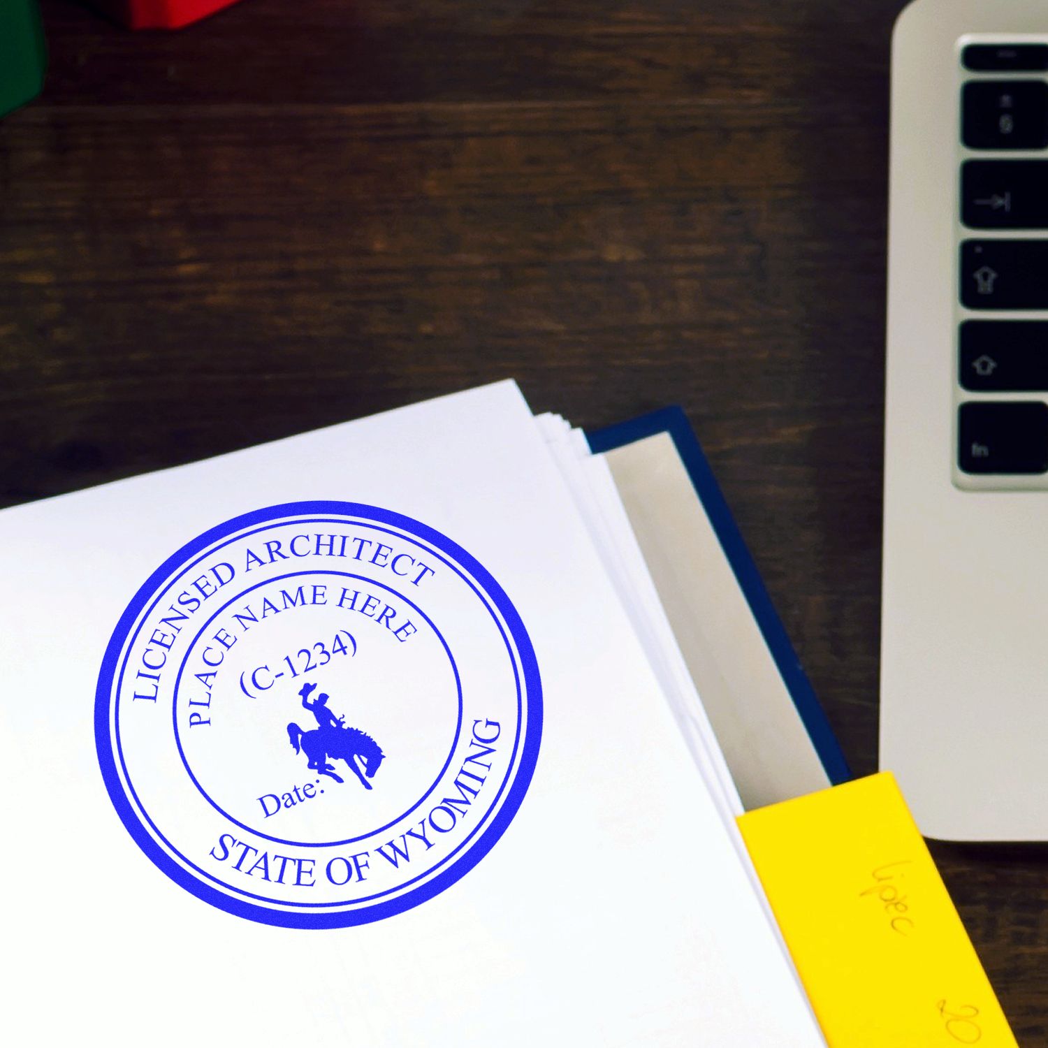 Self Inking Wyoming Architect Stamp imprint on white paper near a laptop on a wooden desk.