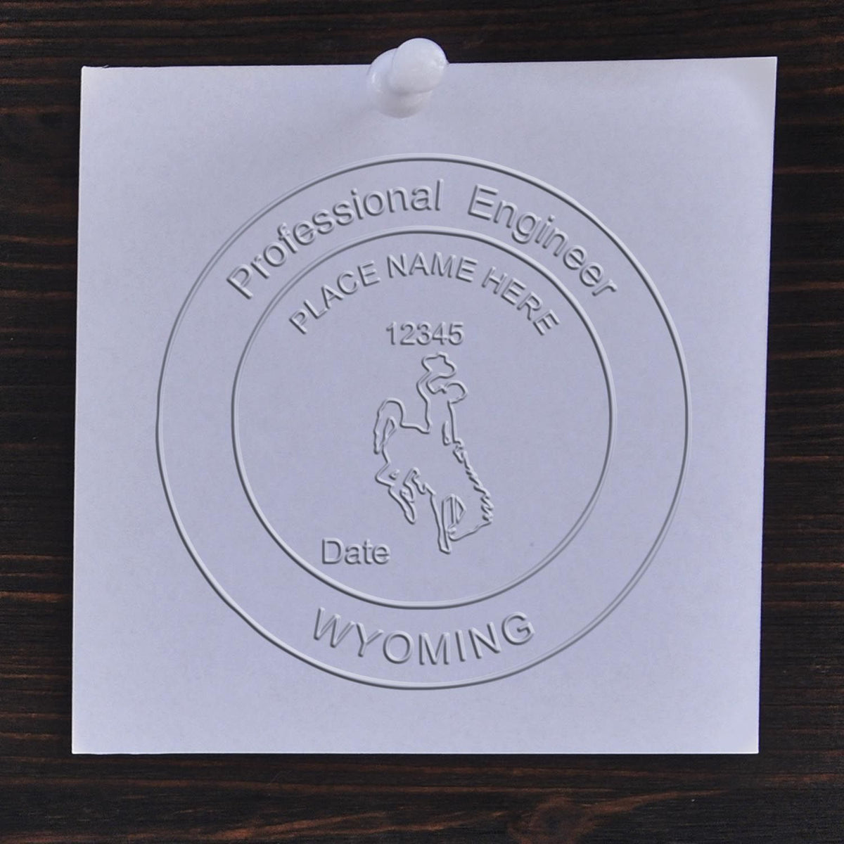A lifestyle photo showing a stamped image of the Handheld Wyoming Professional Engineer Embosser on a piece of paper