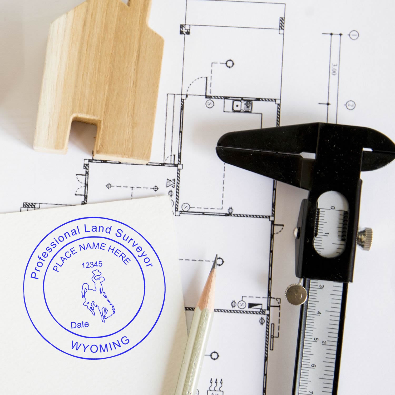 Self Inking Wyoming Land Surveyor Stamp on paper with architectural plans, a pencil, a caliper, and a small wooden house model.