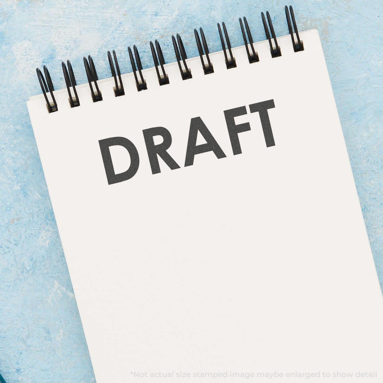 A Black Draft Xstamper Stamp imprinting the word DRAFT on a white spiral notebook against a blue background.