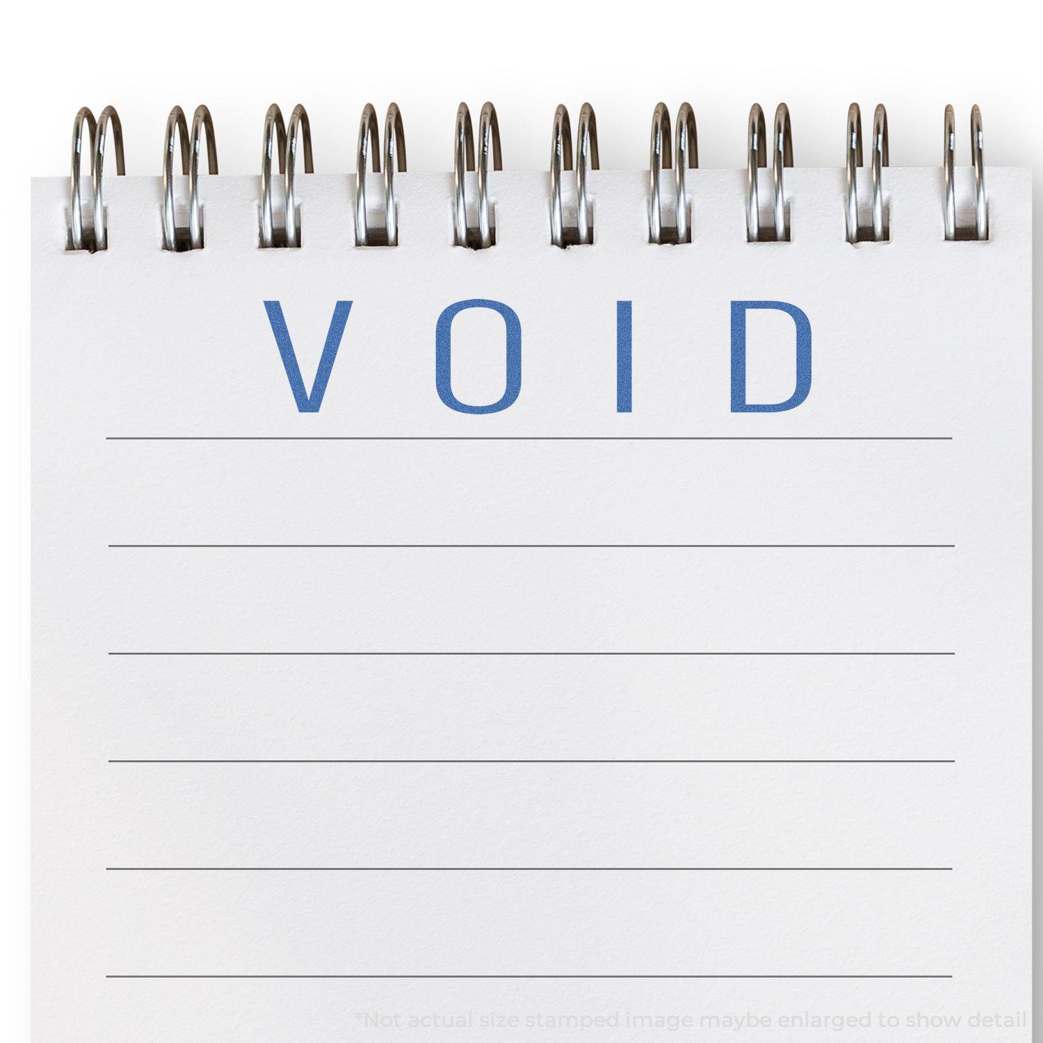 Blue Void Xstamper Stamp imprint on a spiral notebook page, displaying the word "VOID" in blue ink.