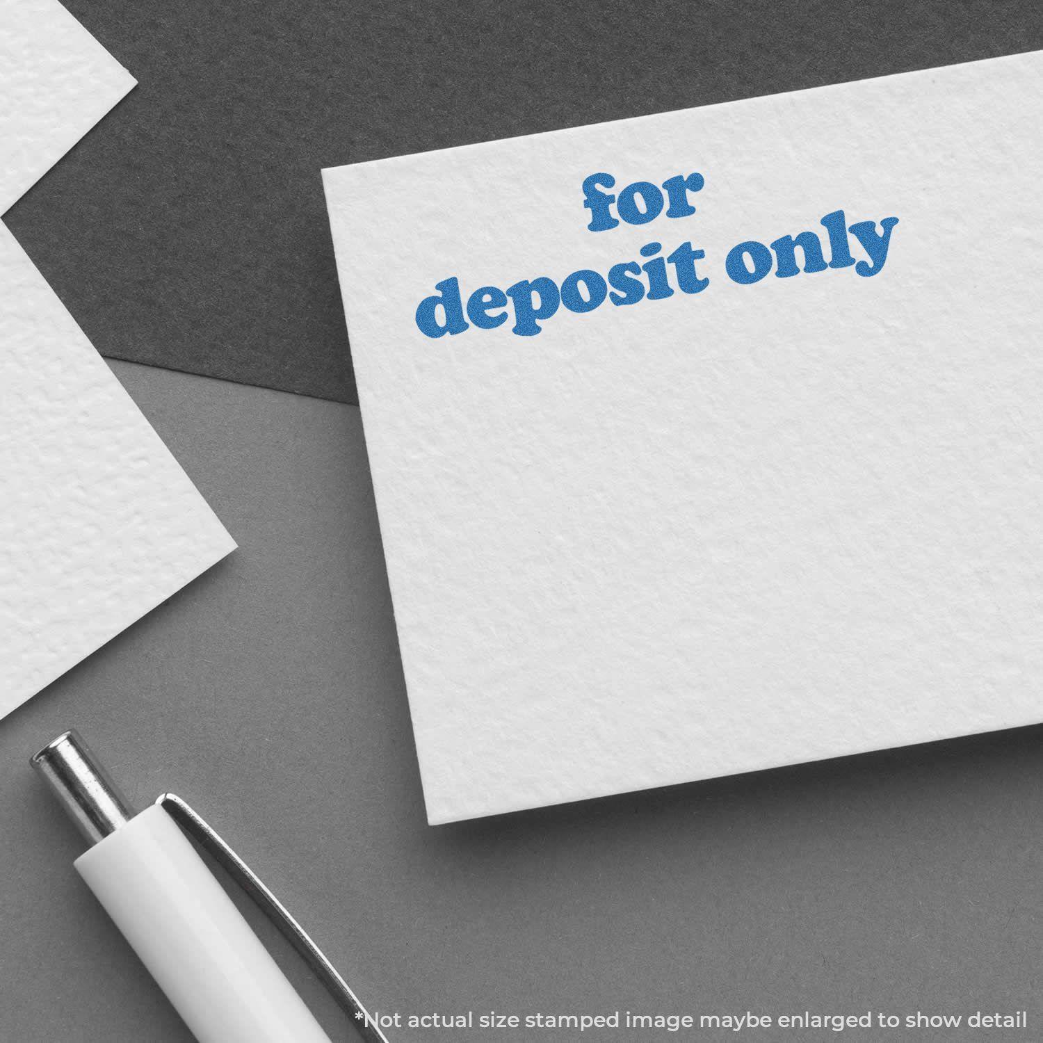 Bold Blue For Deposit Only Xstamper Stamp imprint on white paper, with a pen nearby on a gray background.