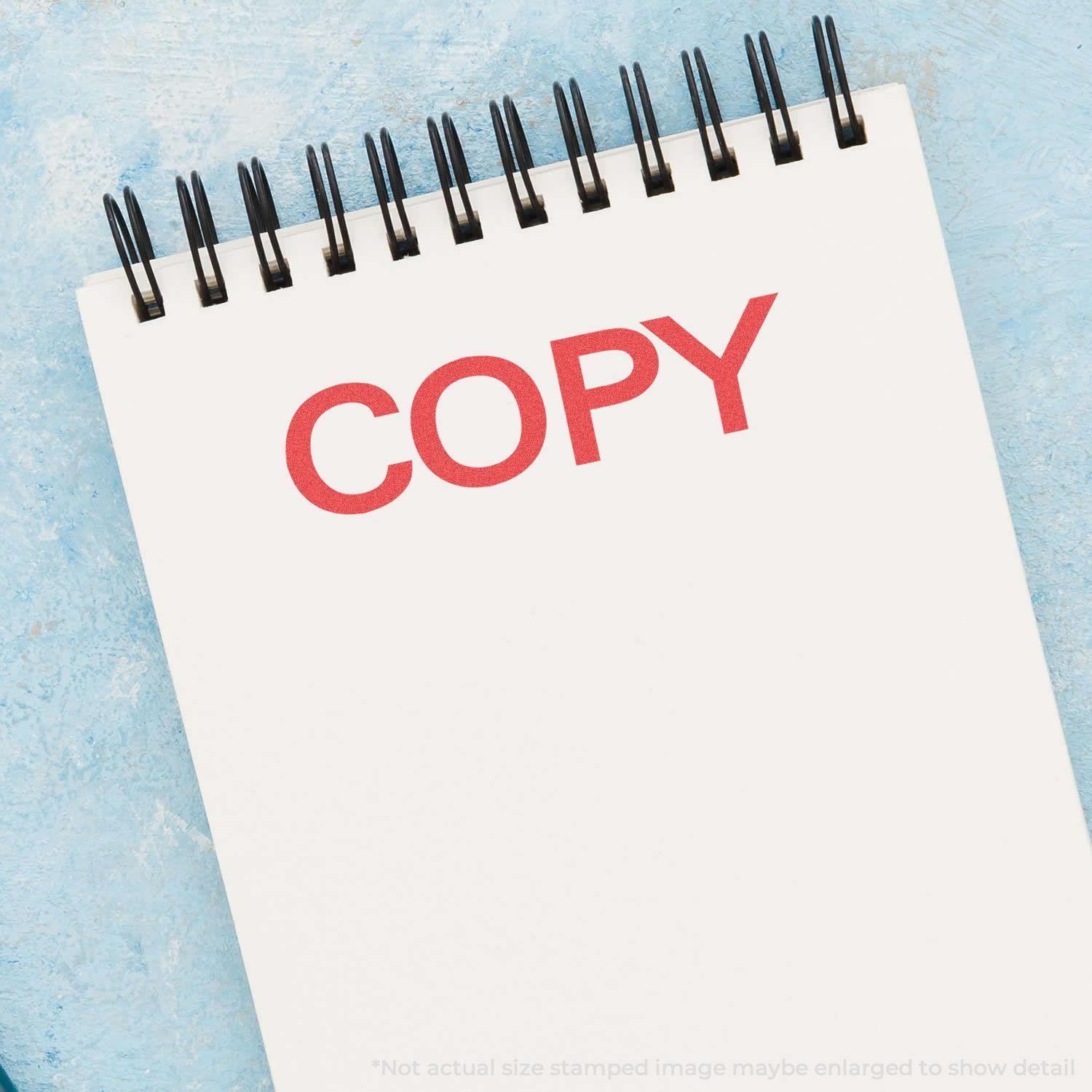 Bold Red Copy Xstamper Stamp imprinting the word COPY in red ink on a white notepad with a blue background.