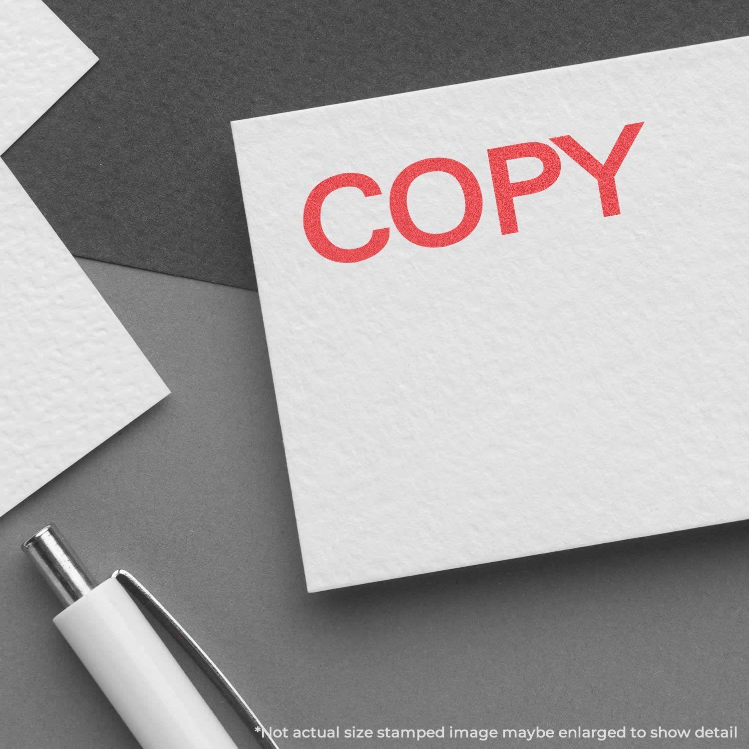 Bold Red Copy Xstamper Stamp imprinting COPY in red on white paper, with a pen nearby on a gray surface.