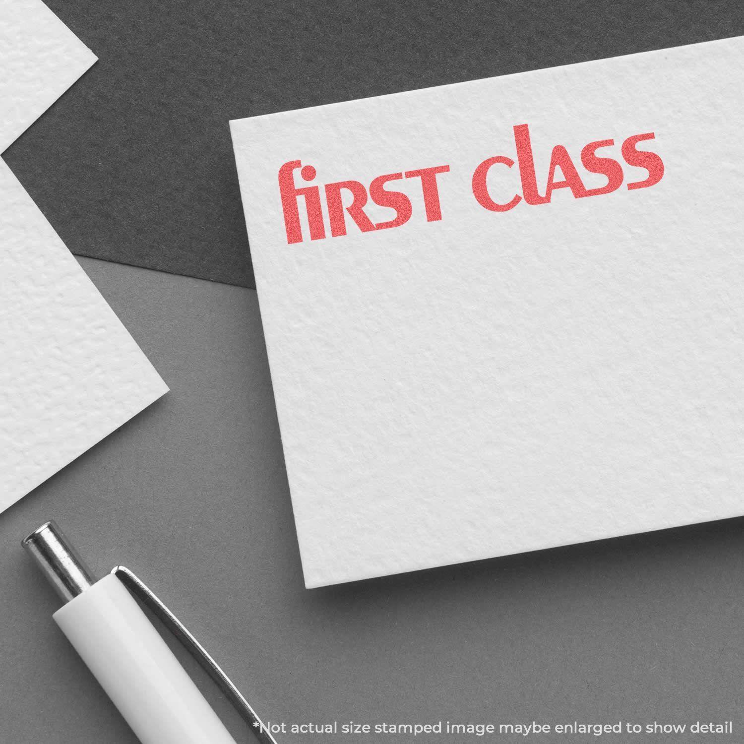 Bold Red First Class Xstamper Stamp imprint on white paper, with a pen and additional papers in the background.