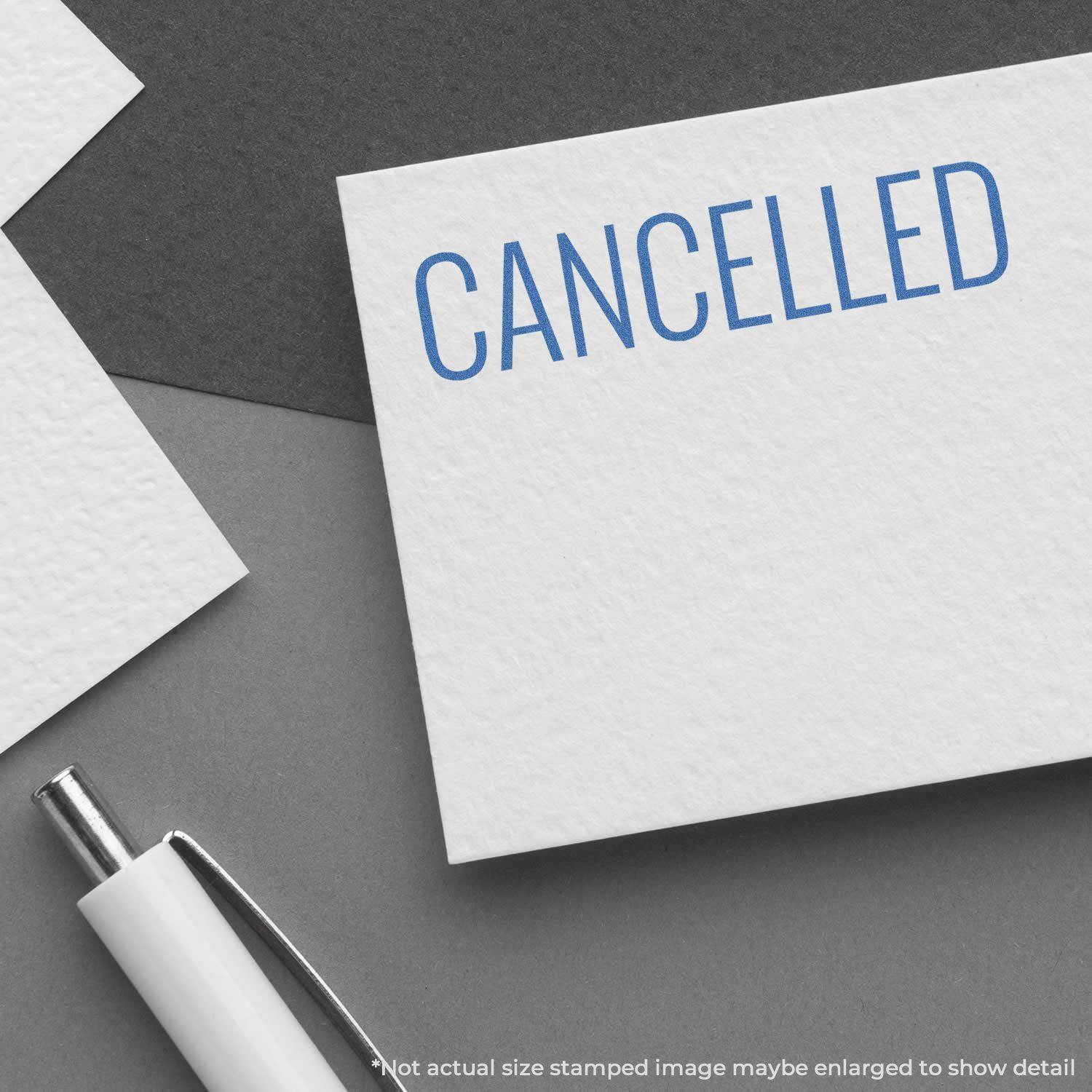 Cancelled Xstamper Stamp in blue ink on a white card, placed on a dark surface with a white pen nearby.