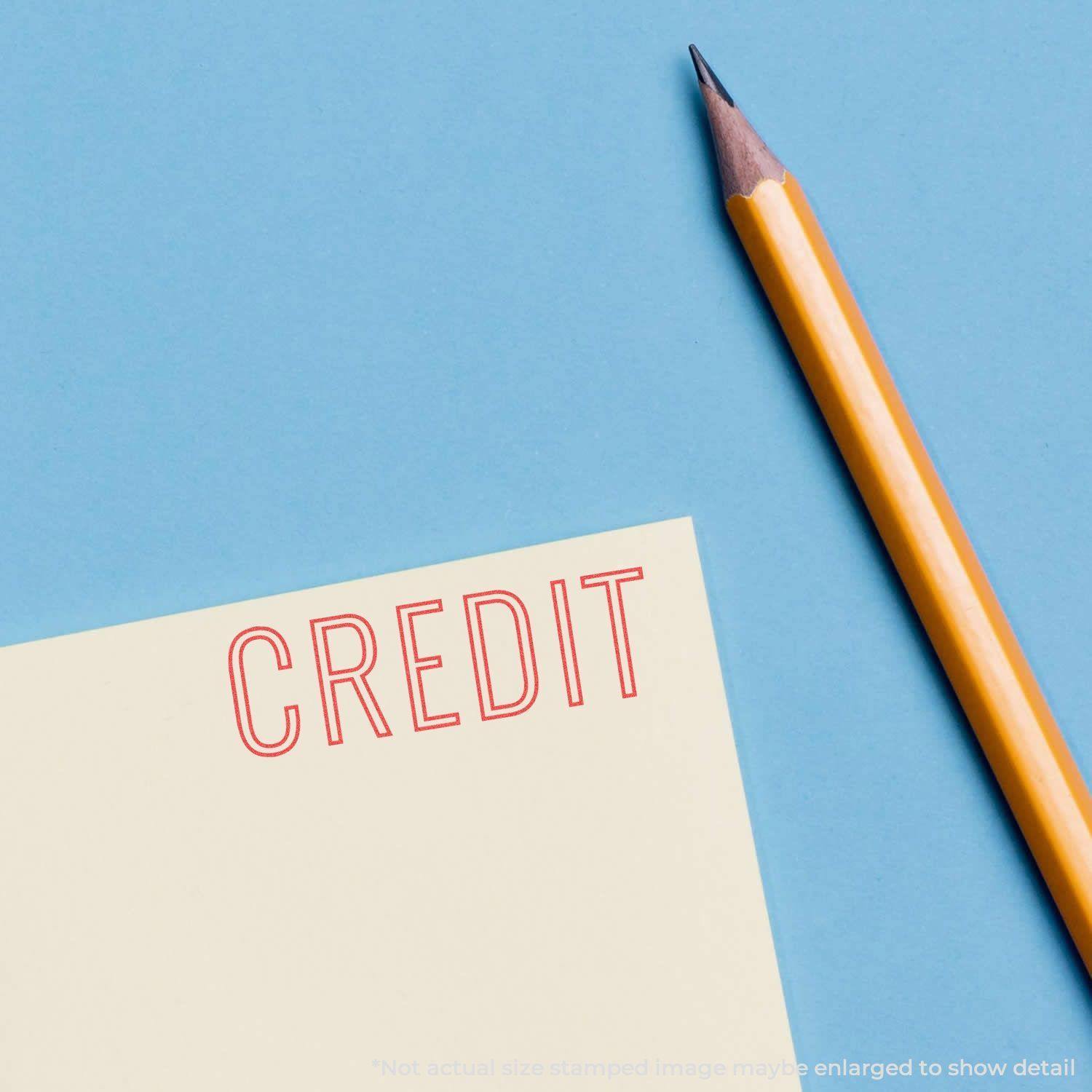 A yellow pencil next to a paper stamped with the word CREDIT in red ink using the Credit Xstamper Stamp on a blue background.