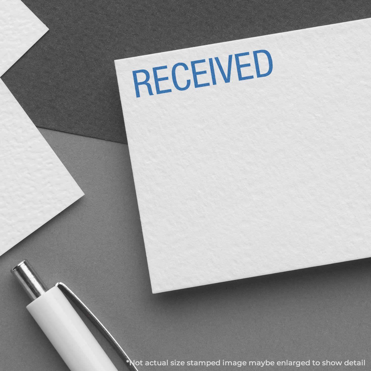 Dark Blue Received Xstamper Stamp marking 'RECEIVED' in blue ink on a white card, with a pen nearby on a dark background.