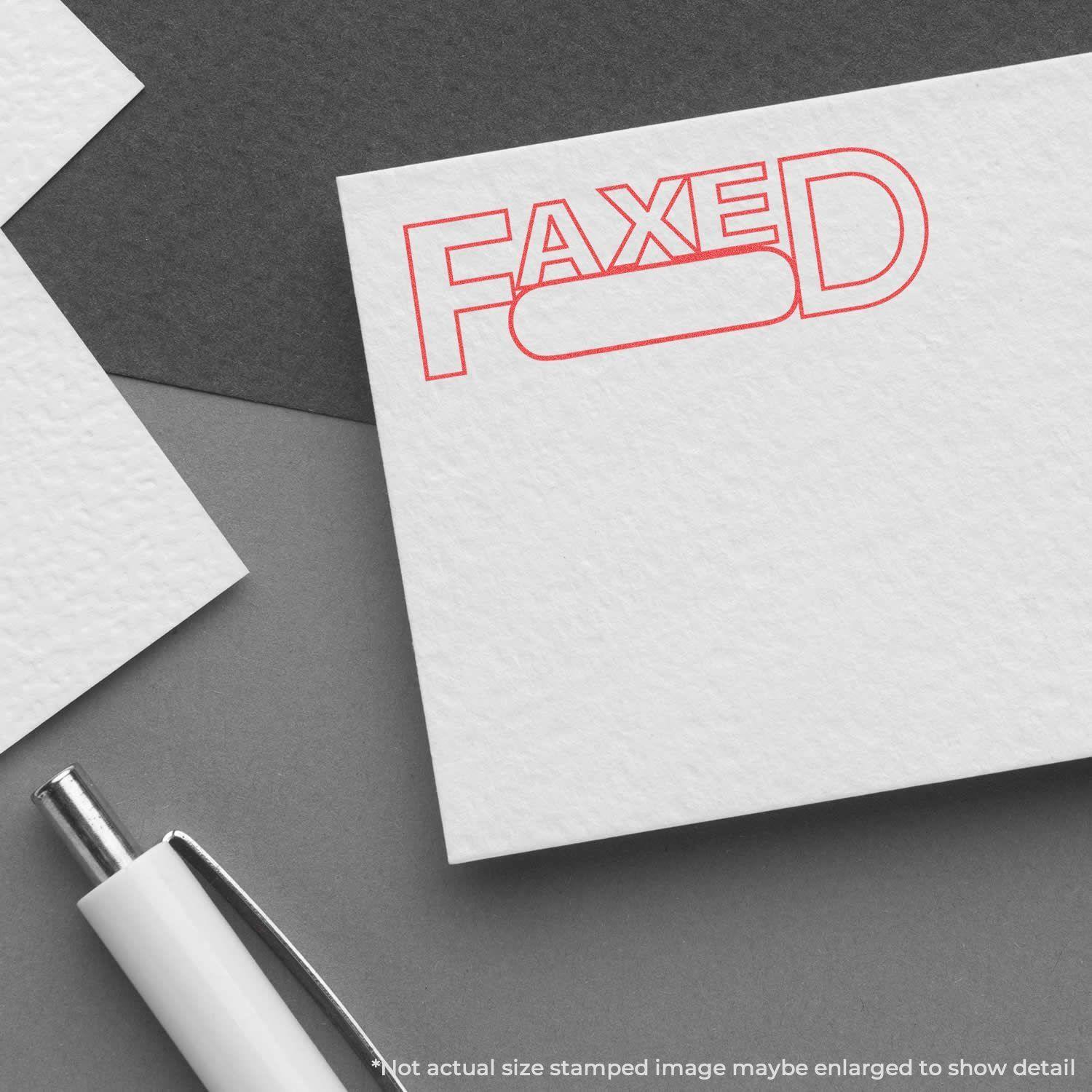 A white card stamped with FAXED in red using the Date Faxed Xstamper Stamp, placed on a gray surface with a white pen nearby.