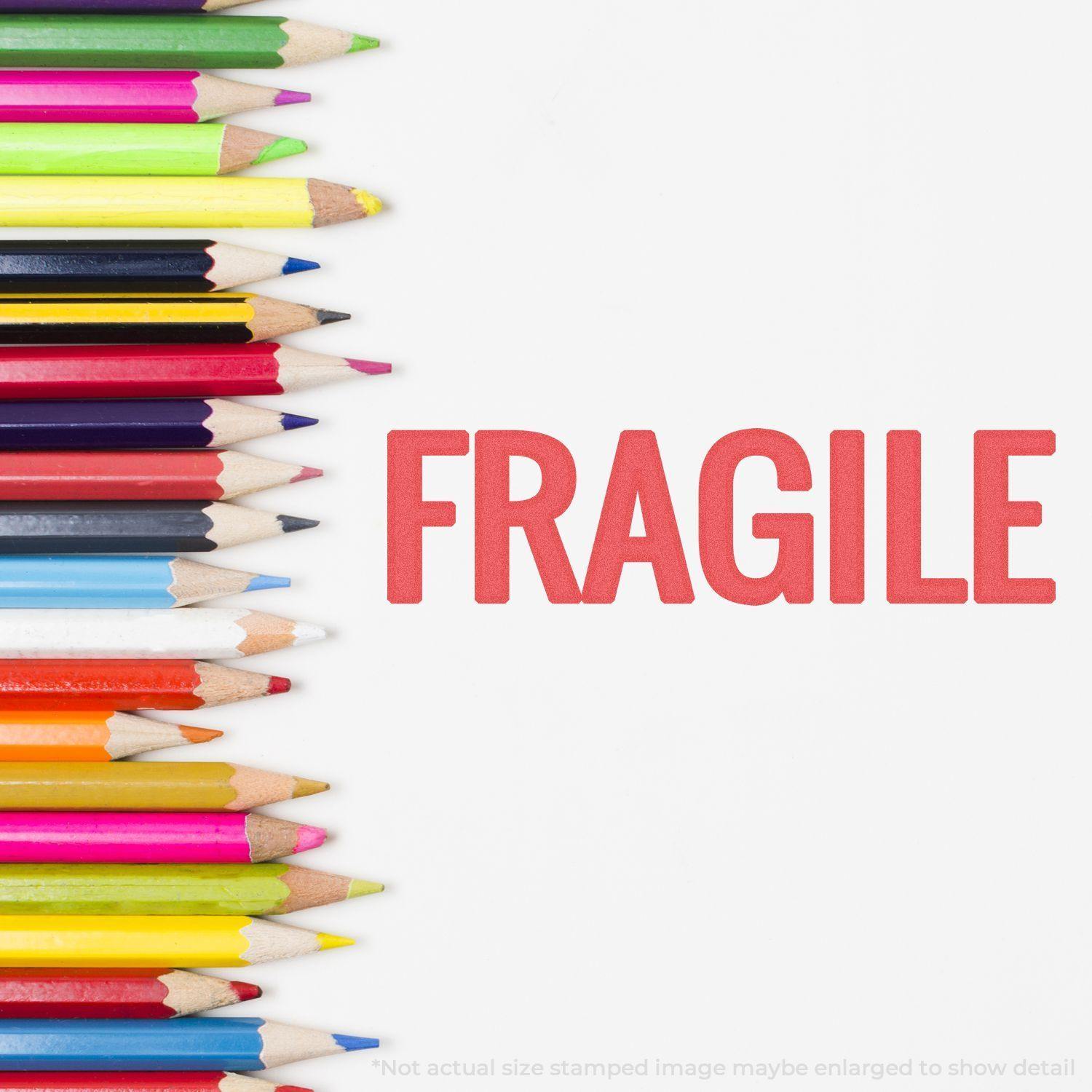 Jumbo Bold Red Fragile Xstamper Stamp imprint reading 'FRAGILE' next to a row of colorful pencils on a white background.