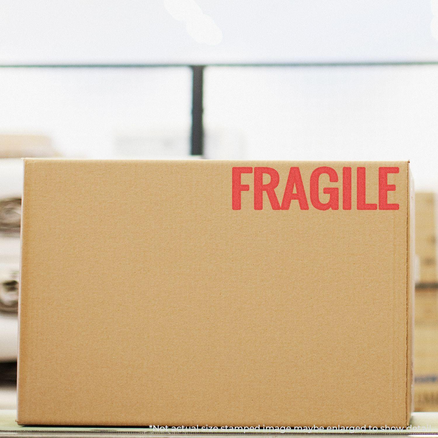 Cardboard box stamped with FRAGILE in bold red letters using the Jumbo Bold Red Fragile Xstamper Stamp, placed in a warehouse setting.