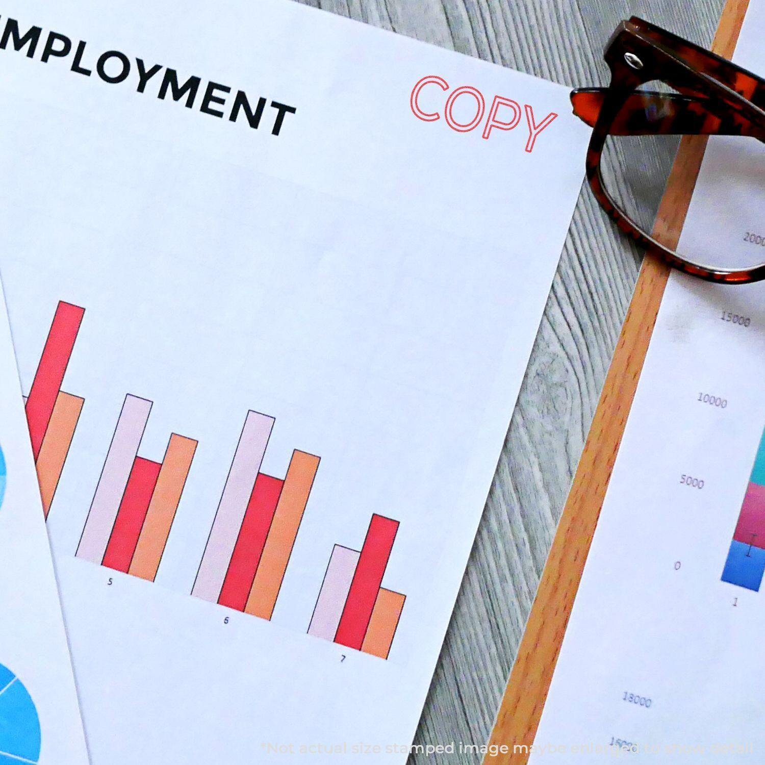 Jumbo Red Copy Xstamper Stamp used on a document with charts and graphs, next to glasses on a wooden desk.