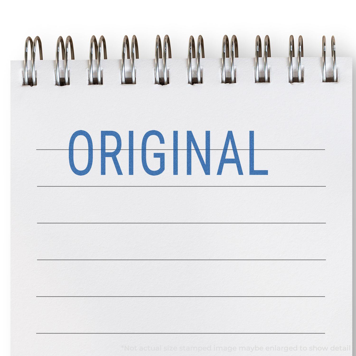 Original Xstamper Stamp imprint on a spiral-bound notebook, showing the word ORIGINAL in blue ink on lined paper.