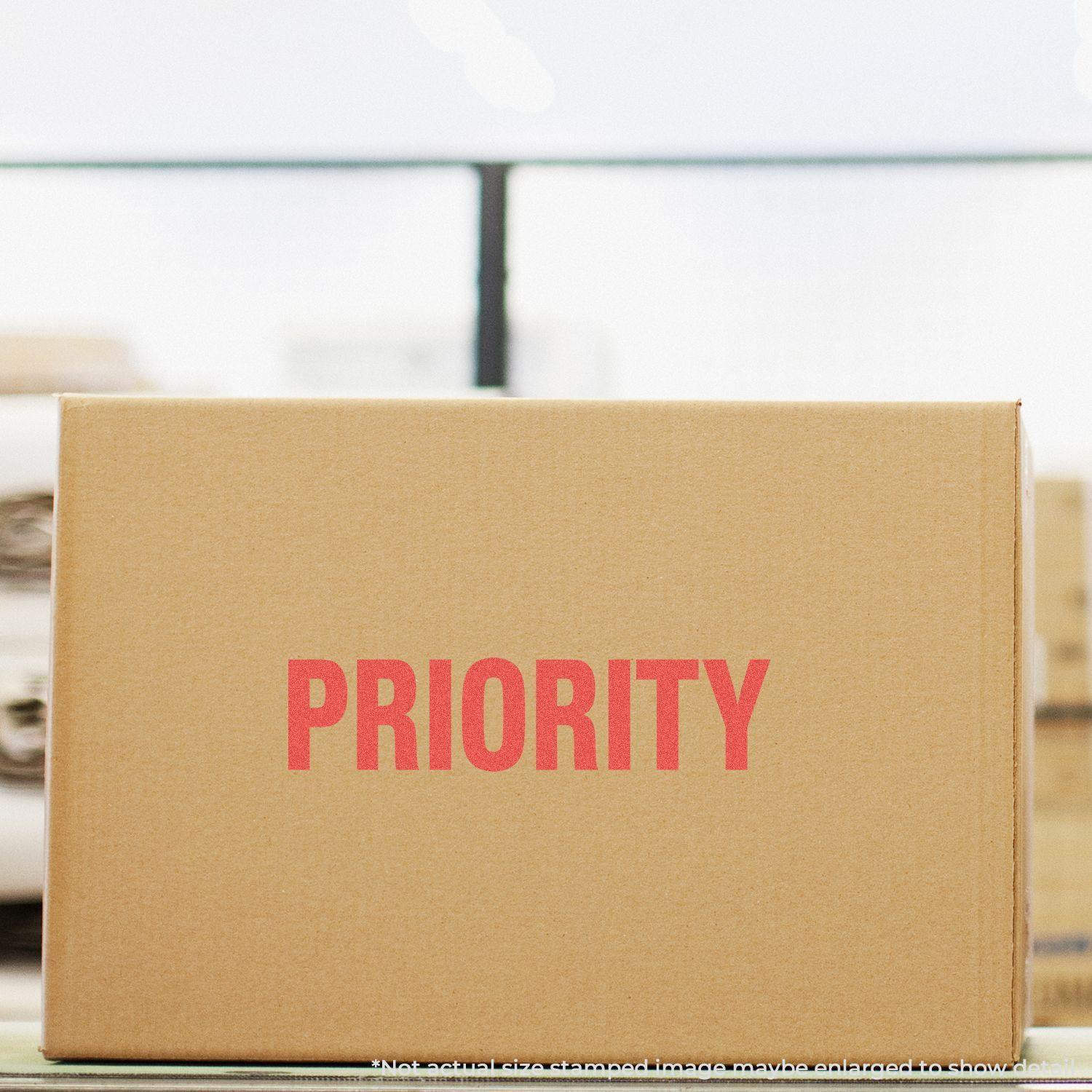 Cardboard box stamped with PRIORITY in red using the Priority Xstamper Stamp, placed in a warehouse setting.