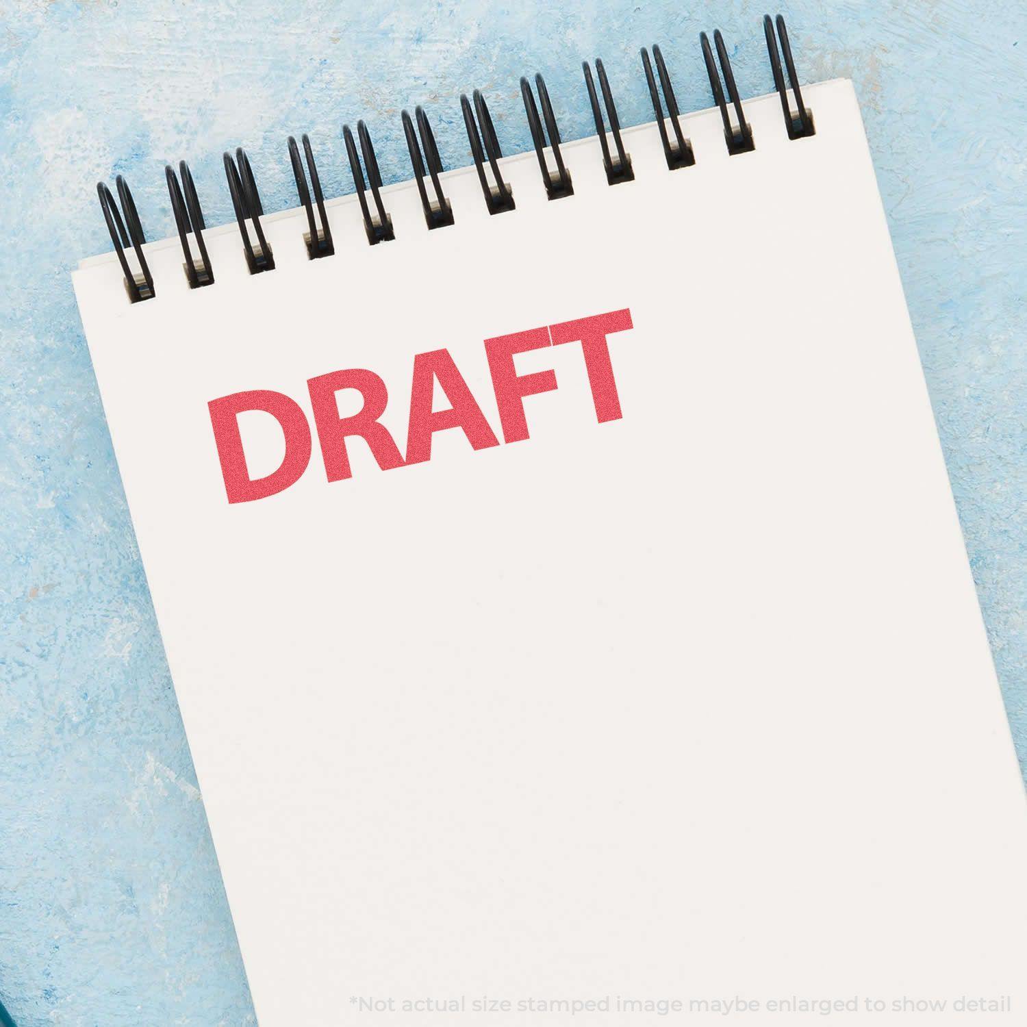 A Red Draft Xstamper Stamp imprint on a white spiral notebook, displaying the word DRAFT in bold red letters against a blue background.