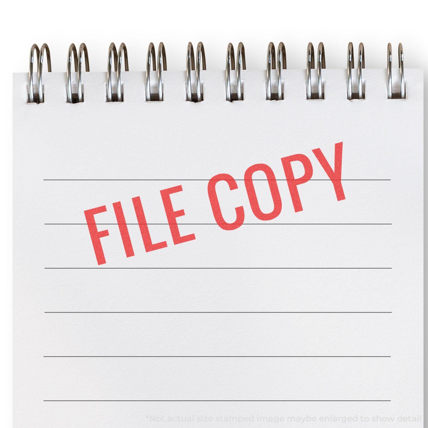 Red File Copy Xstamper Stamp imprinting FILE COPY in red ink on a white, spiral-bound notepad with lined pages.