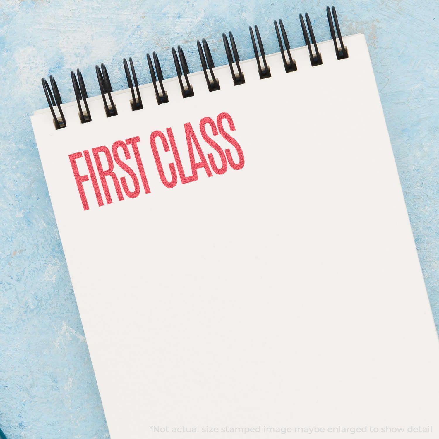 Red First Class Xstamper Stamp imprinting FIRST CLASS in red ink on a white notepad with a blue background.