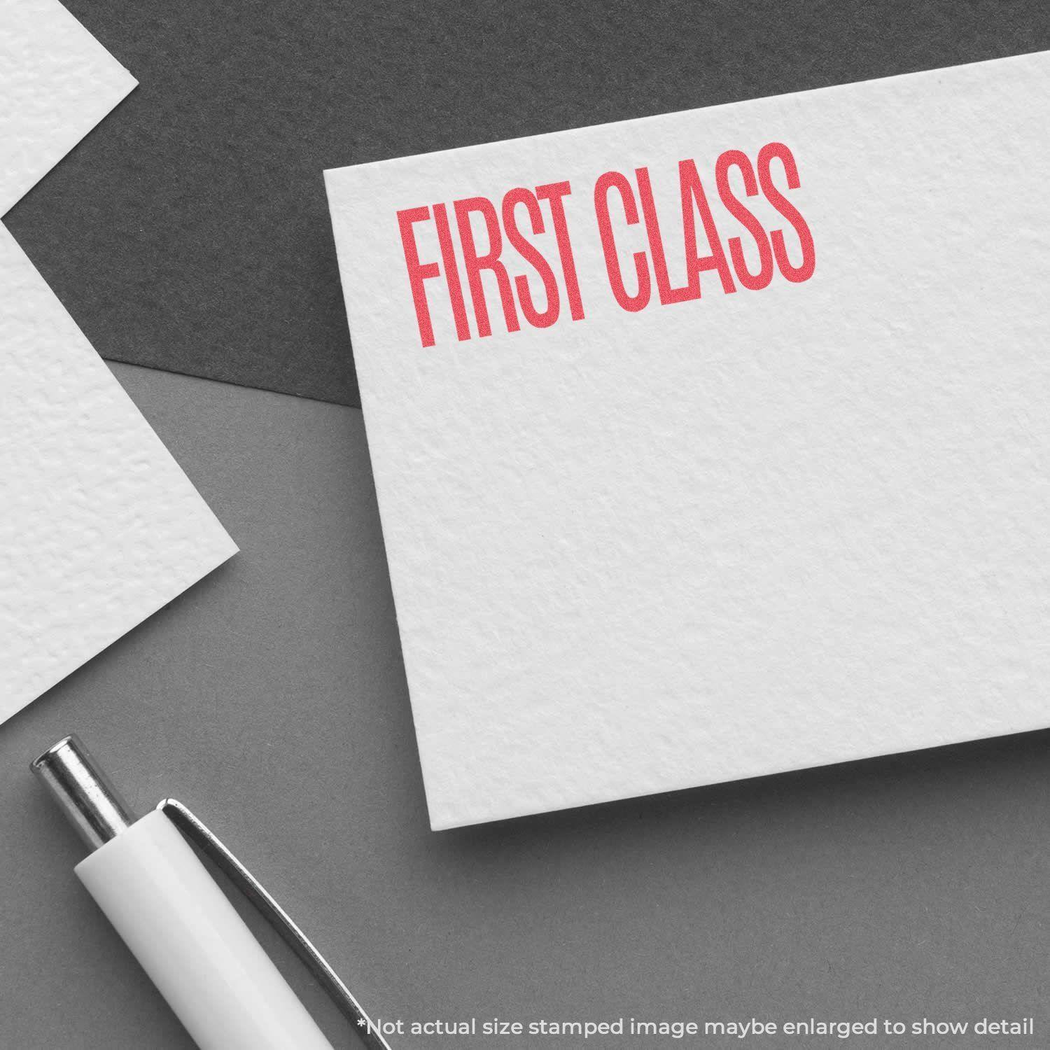 Red First Class Xstamper Stamp imprint on white paper, next to a white pen on a gray surface.