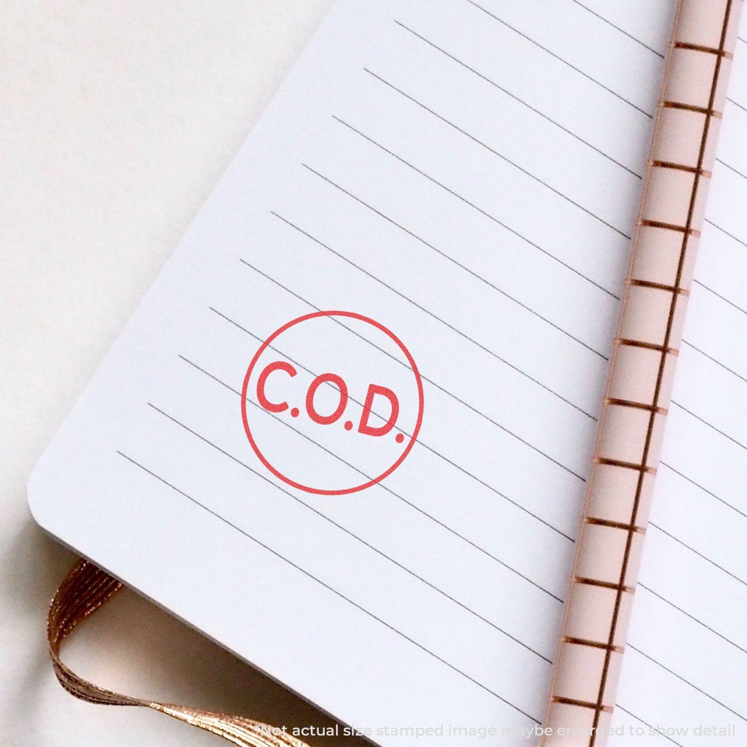 Round C.O.D. Xstamper Stamp in red ink on a lined notebook page with a spiral binding.