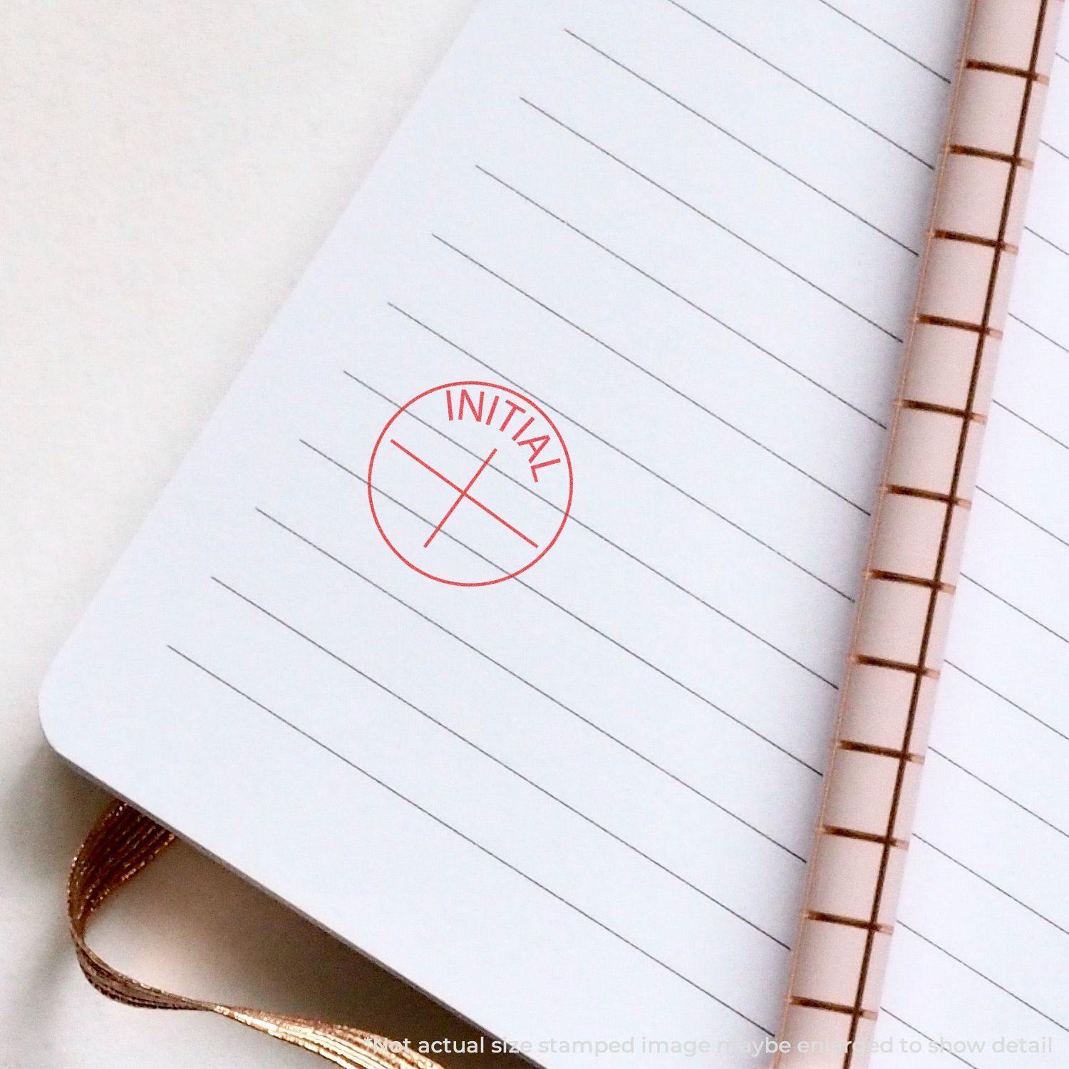 Round Initial Xstamper Stamp imprint in red ink on a lined notebook page, showing the word INITIAL within a circular border.