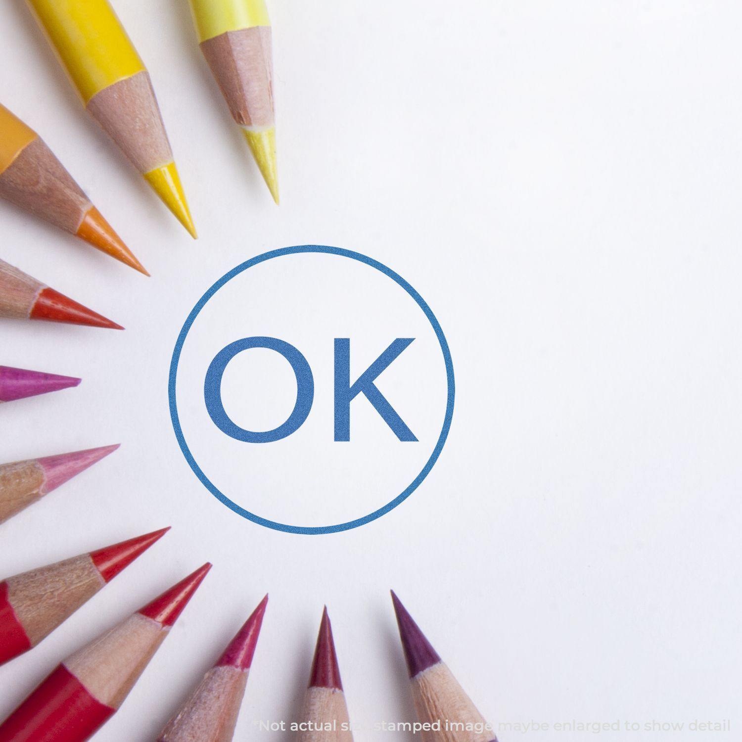 Round Ok Xstamper Stamp imprint on white paper surrounded by colored pencils arranged in a circle.