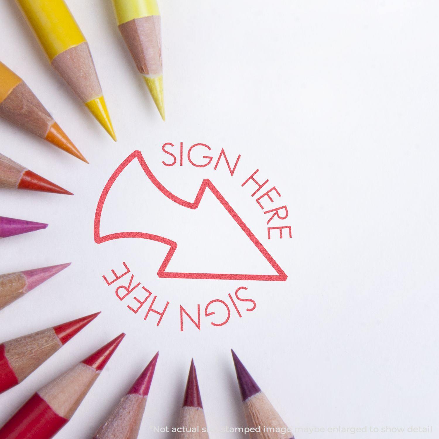 Round Red Sign Here Xstamper Stamp impression on paper, surrounded by colorful pencils pointing towards the stamped image.