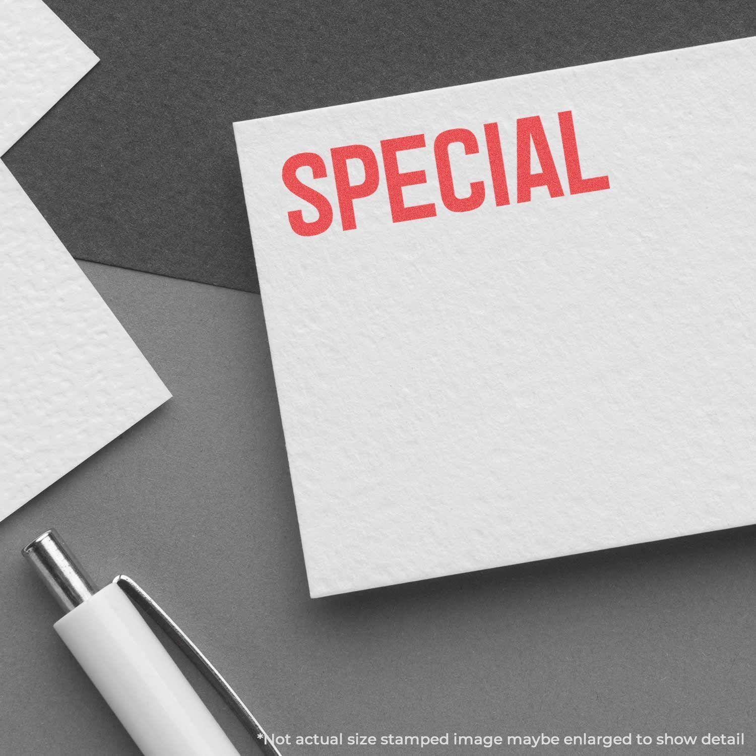 A white card stamped with SPECIAL in red ink using the Special Xstamper Stamp, placed on a gray surface beside a white pen.