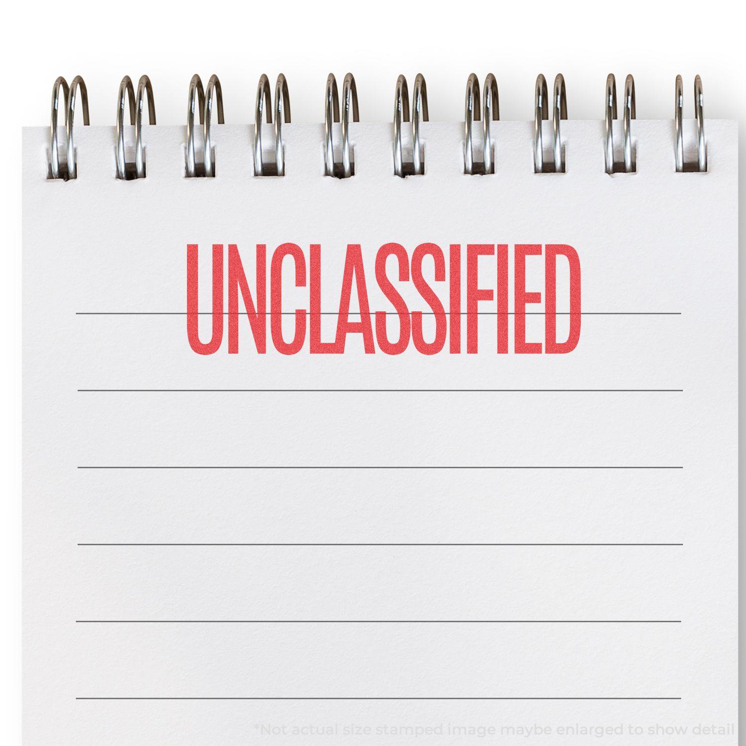 Unclassified Xstamper Stamp imprint in red ink on a white notepad with spiral binding, displaying the word 'UNCLASSIFIED' in bold letters.